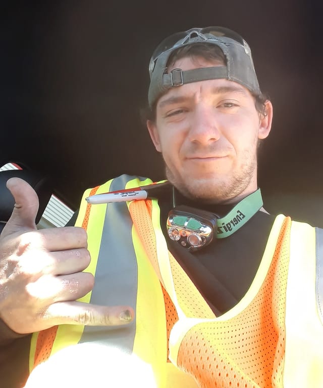 Andy in a hi-vis vest and backwards cap, throwing a shaka