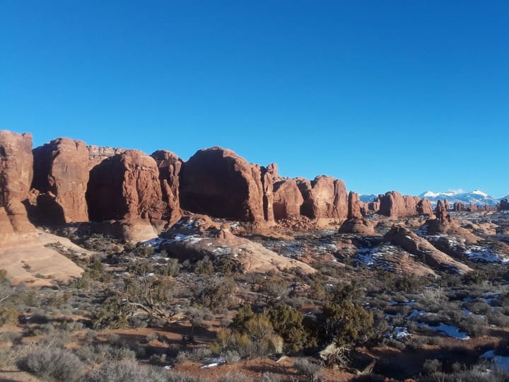 Red sandstone fins and a snow-dusted desert floor with the La Sal Mountains in the distance