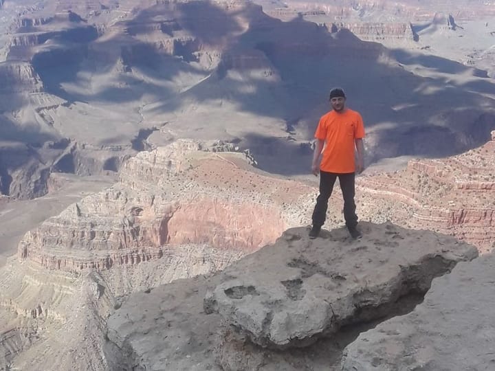 Standing on a ledge of limestone above the canyon in an orange shirt
