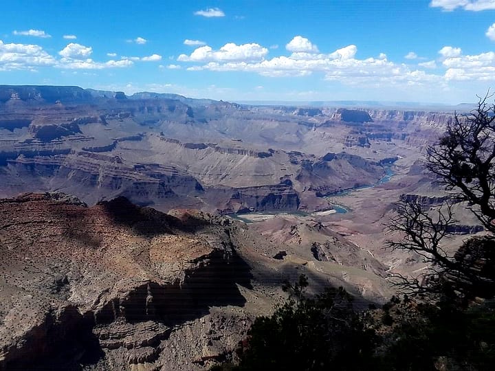 The Grand Canyon stretching away under a blue sky, with the Colorado River winding through it