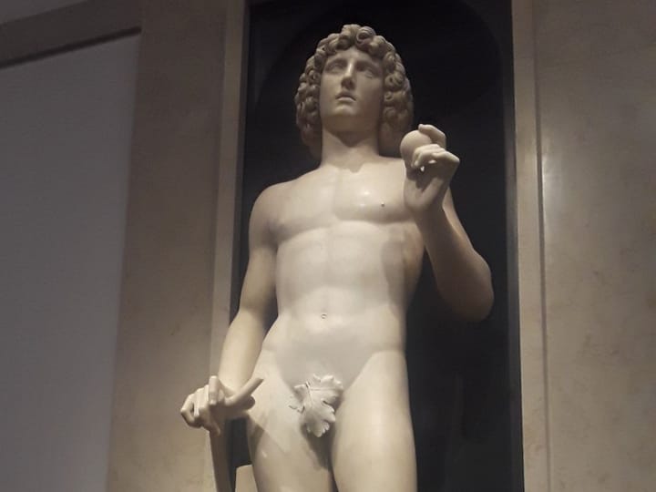 A marble statue of Adam holding an apple, standing in a dark niche at the Met