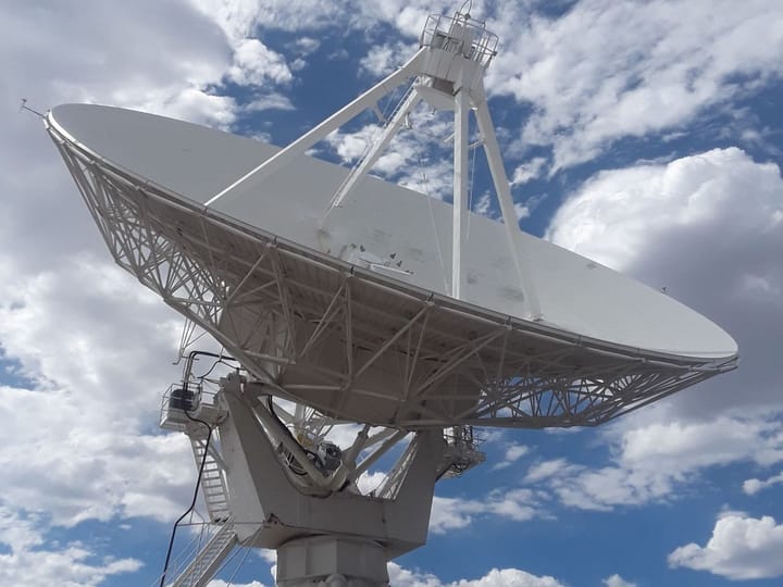 A Very Large Array dish tilted against a cloudy sky