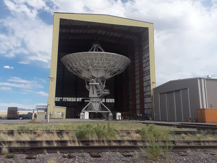 A radio dish sitting inside its maintenance building at the end of the rails