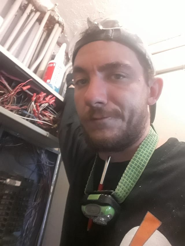 Andy next to an open wiring panel, headlamp around his neck
