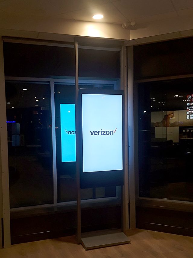 A Verizon digital signage kiosk lit up in a dark storefront at night